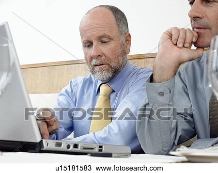Stock Image - Businessmen using laptop indoors. Fotosearch