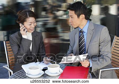 Stock Image - Businesspeople Meeting at outdoor Cafe talking on phone reviewing documents. Fotosearch