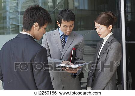 Stock Photograph - Businesspeople standing outside looking over documents. Fotosearch