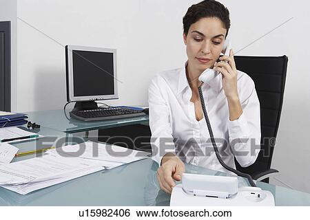 Stock Photograph - Businesswoman dialling telephone in office. Fotosearch
