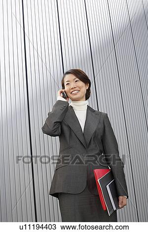 Stock Image - Businesswoman holding paperwork using Cell Phone. Fotosearch
