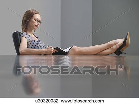 Businesswoman sitting and studying book feet on table side view View Large Photo Image Stock Image - Businesswoman sitting and studying book feet on table side view. Fotosearch