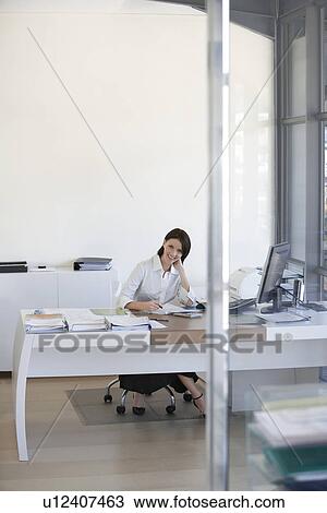 Stock Image - Businesswoman sitting at desk in office.. Fotosearch