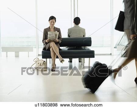 Stock Photo - Businesswoman sitting on bench in airport reading newspaper. Fotosearch