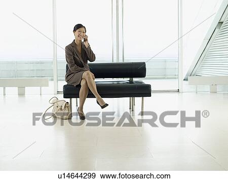 Stock Photo - Businesswoman Sitting on Bench in airport talking on mobile. Fotosearch