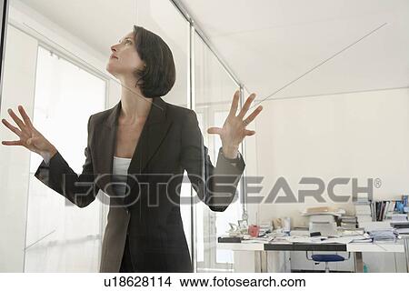 Picture - Businesswoman standing in office pressing hands and face against glass.. Fotosearch