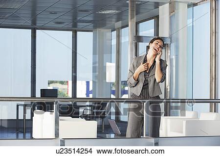 Picture - Businesswoman standing in office talking on mobile phone. Fotosearch