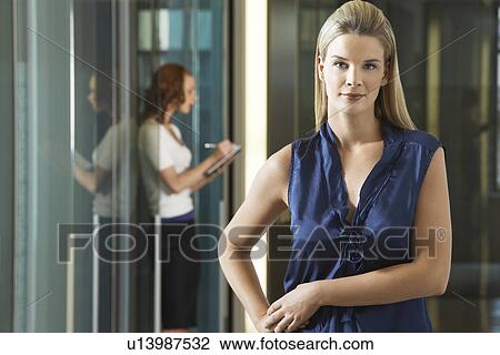 Stock Image - Businesswoman standing in office corridor portrait. Fotosearch