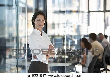 Stock Photo - Businesswoman standing in office with group of office workers in background.. Fotosearch