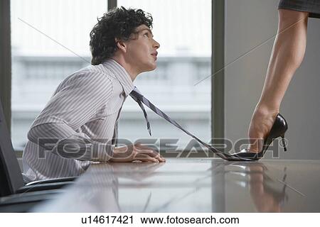 Stock Image - Businesswoman standing on desk stepping on businessman's tie side view. Fotosearch