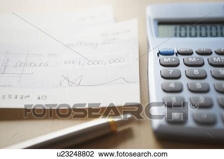 Stock Image - Calculator pen and filled cheque on table close-up. Fotosearch