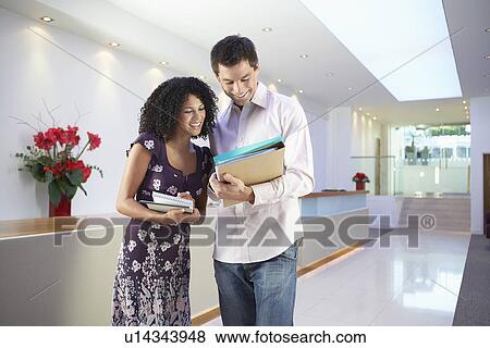 Casually dressed office workers standing looking over paperwork View Large Photo Image Stock Photo - Casually dressed office workers standing looking over paperwork. Fotosearch