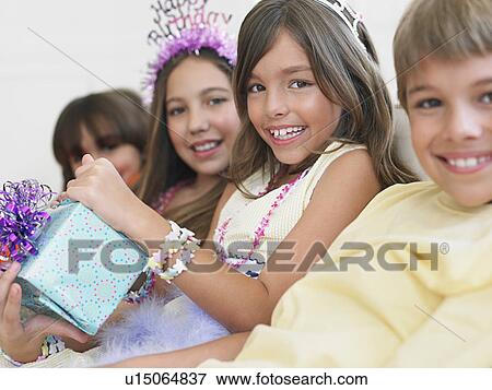 Stock Photo - Children (7-12) sitting in row at birthday party one holding present. Fotosearch