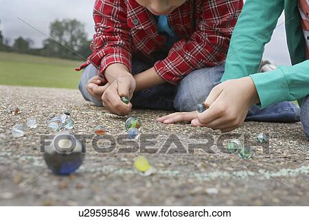 Stock Photograph - Children (7-9) playing marbles lying in playground. Fotosearch