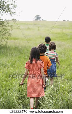 Stock Image - Children (7-9) walking in field. Fotosearch