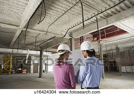 Picture - Construction manager and architect examining plans on site back view. Fotosearch