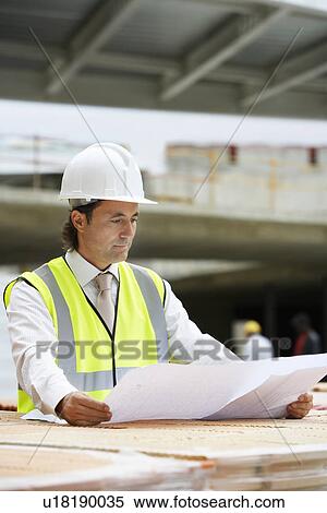 Stock Photography - Construction worker examining building plans on site. Fotosearch
