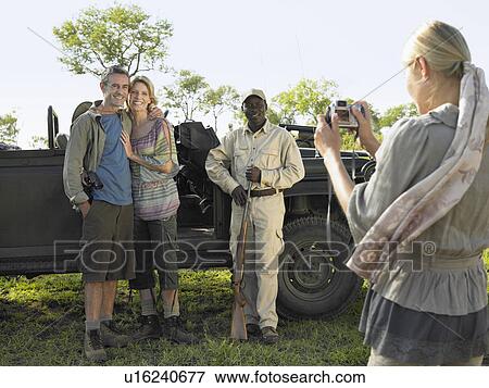Stock Photo - Couple and safari guide posing by jeep young woman taking photograph. Fotosearch