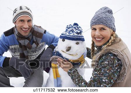 Stock Image - Couple dressing snowman crouching in snow portrait. Fotosearch