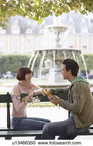 Stock Image - Couple Eating Baguettes in Park. Fotosearch