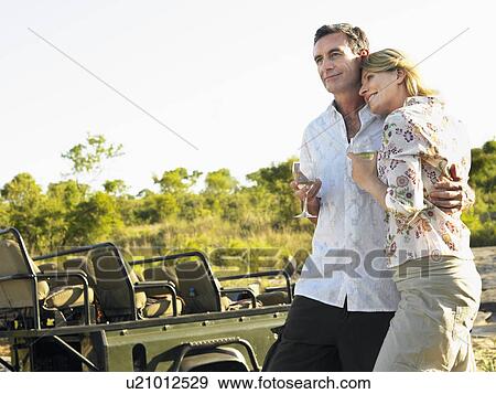 Couple embracing holding wineglasses smiling jeep in background View Large Photo Image Stock Photo - Couple embracing holding wineglasses smiling jeep in background. Fotosearch