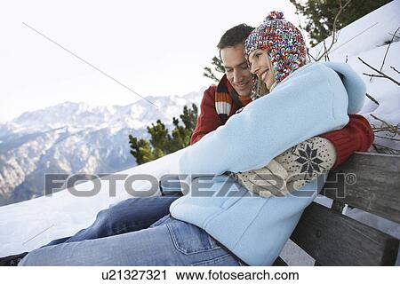 Stock Image - Couple embracing sitting on bench on hillside side view. Fotosearch