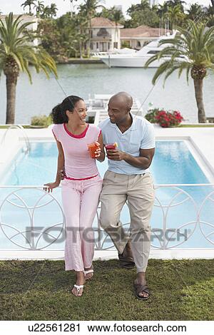 Couple holding cocktails leaning on pool banister elevated view View Large Photo Image Stock Image - Couple holding cocktails leaning on pool banister elevated view. Fotosearch