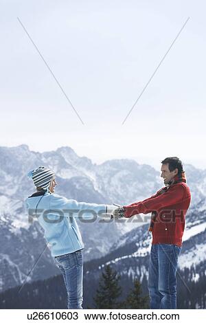 Stock Image - Couple holding hands standing face to face in mountains side view. Fotosearch