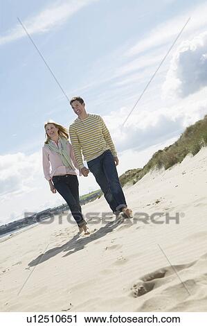 Stock Image - Couple holding hands walking on beach. Fotosearch