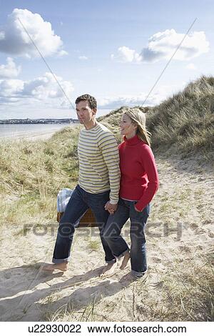 Couple holding hands walking on sand dune View Large Photo Image Stock Image - Couple holding hands walking on sand dune. Fotosearch