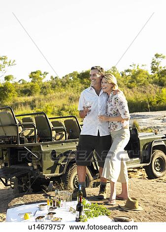Stock Photo - Couple on picnic during safari smiling jeep in background. Fotosearch