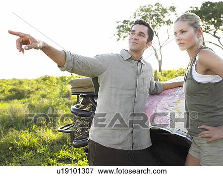 Stock Photo - Couple on safari man pointing map on jeep. Fotosearch