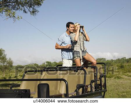 Couple on safari standing in jeep woman looking through binoculars View Large Photo Image Picture - Couple on safari standing in jeep woman looking through binoculars. Fotosearch