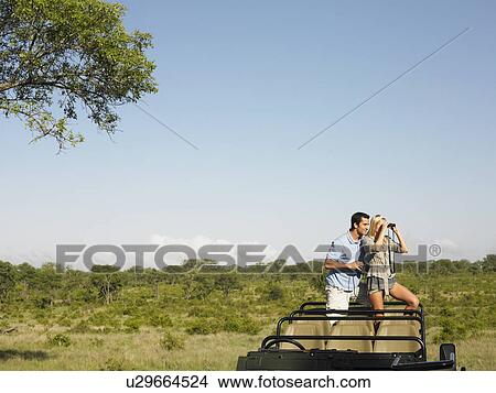 Couple on safari standing in jeep woman looking through binoculars View Large Photo Image Picture - Couple on safari standing in jeep woman looking through binoculars. Fotosearch