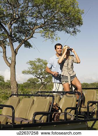 Stock Photo - Couple on safari standing in jeep woman looking through binoculars. Fotosearch