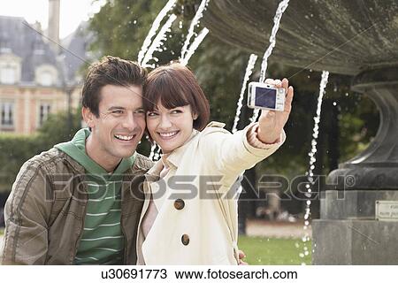 Stock Image - Couple photographing themselves in front of fountain. Fotosearch