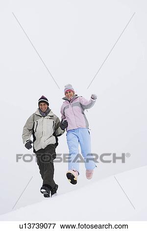 Couple running down snow-covered hill low angle view View Large Photo Image Stock Photo - Couple running down snow-covered hill low angle view. Fotosearch