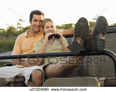 Stock Image - Couple sitting in jeep woman holding binoculars. Fotosearch