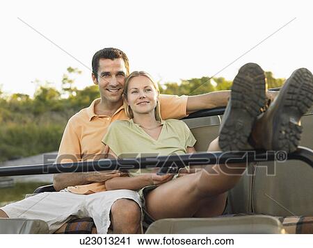 Stock Image - Couple sitting in jeep woman leaning legs up. Fotosearch