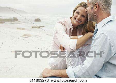 Stock Photograph - Couple sitting on beach smiling. Fotosearch
