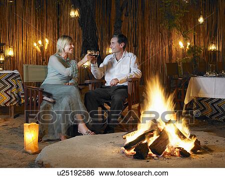Couple sitting on chairs at outdoor nightclub near bonfire toasting View Large Photo Image Stock Photograph - Couple sitting on chairs at outdoor nightclub near bonfire toasting. Fotosearch