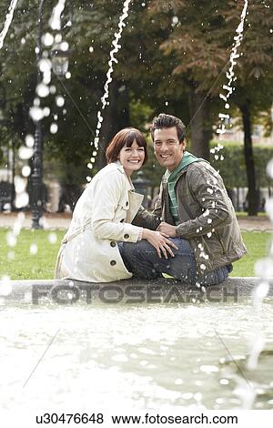 Couple sitting on edge of fountain view past water jets View Large Photo Image Stock Photo - Couple sitting on edge of fountain view past water jets. Fotosearch