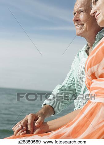 Stock Photo - Couple sitting on edge of pier looking at view side view. Fotosearch