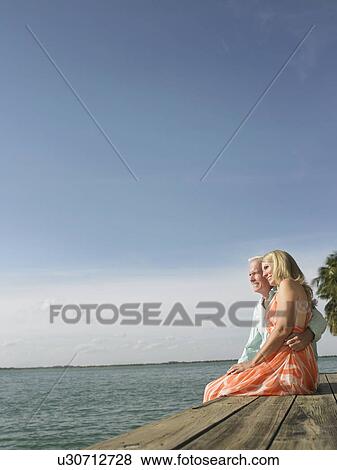 Couple sitting on edge of pier side view View Large Photo Image Stock Photo - Couple sitting on edge of pier side view. Fotosearch