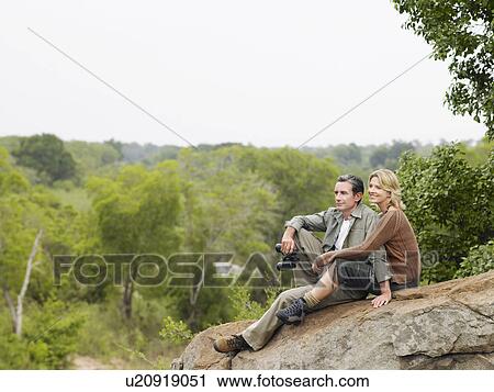 Stock Image - Couple sitting on rock looking at view. Fotosearch