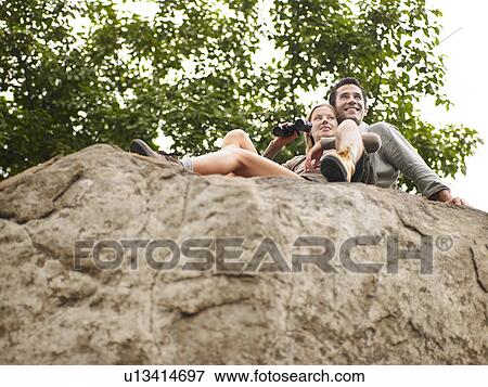 Couple sitting on rock woman holding binoculars. low angle view View Large Photo Image Stock Photo - Couple sitting on rock woman holding binoculars. low angle view. Fotosearch