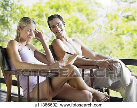 Stock Image - Couple sitting on terrace woman reading book. Fotosearch