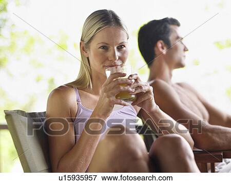 Stock Photo - Couple sitting outdoors woman drinking juice focus on foreground. Fotosearch