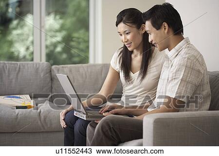 Couple sitting side by side on Sofa Using a Laptop View Large Photo Image Stock Image - Couple sitting side by side on Sofa Using a Laptop. Fotosearch
