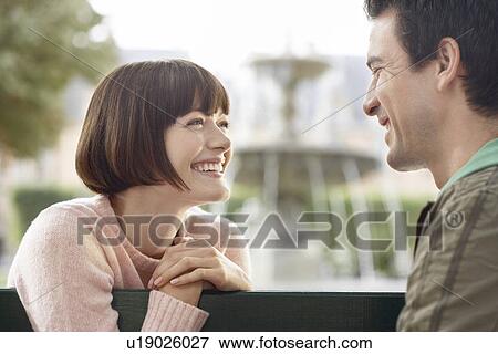 Couple smiling at each other on bench in front of fountain head and shoulders View Large Photo Image Stock Photo - Couple smiling at each other on bench in front of fountain head and shoulders. Fotosearch